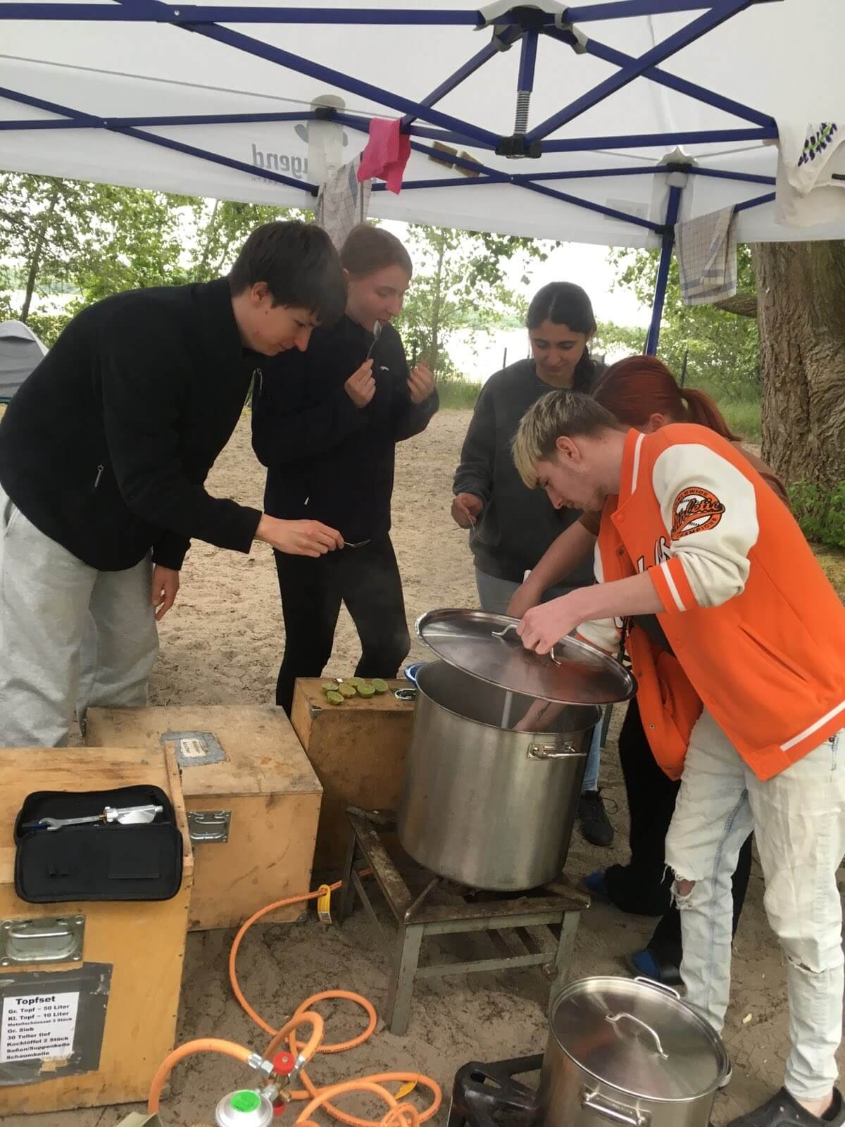 Gruppe kocht draußen unter einem Zelt.